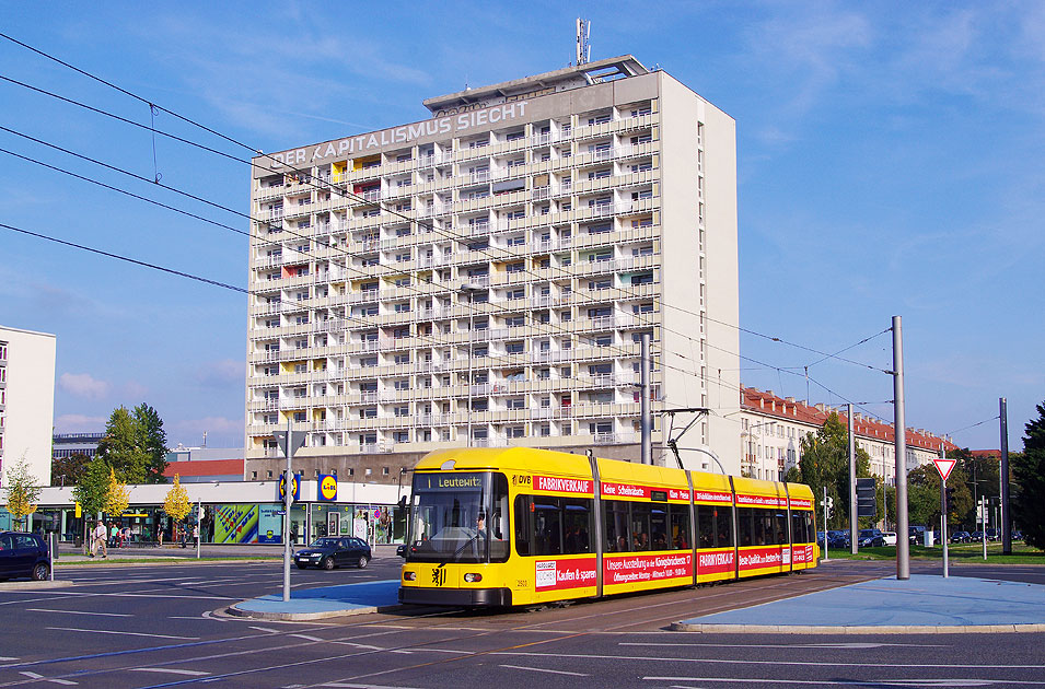 Im Hintergrund das markante Hochhaus Pirnaischer Platz: Die Straßenbahn in Dresden an der Haltestelle Pirnaischer Platz - Parole Der Kapitalismus siecht - vormals: Der Sozialismus siegt